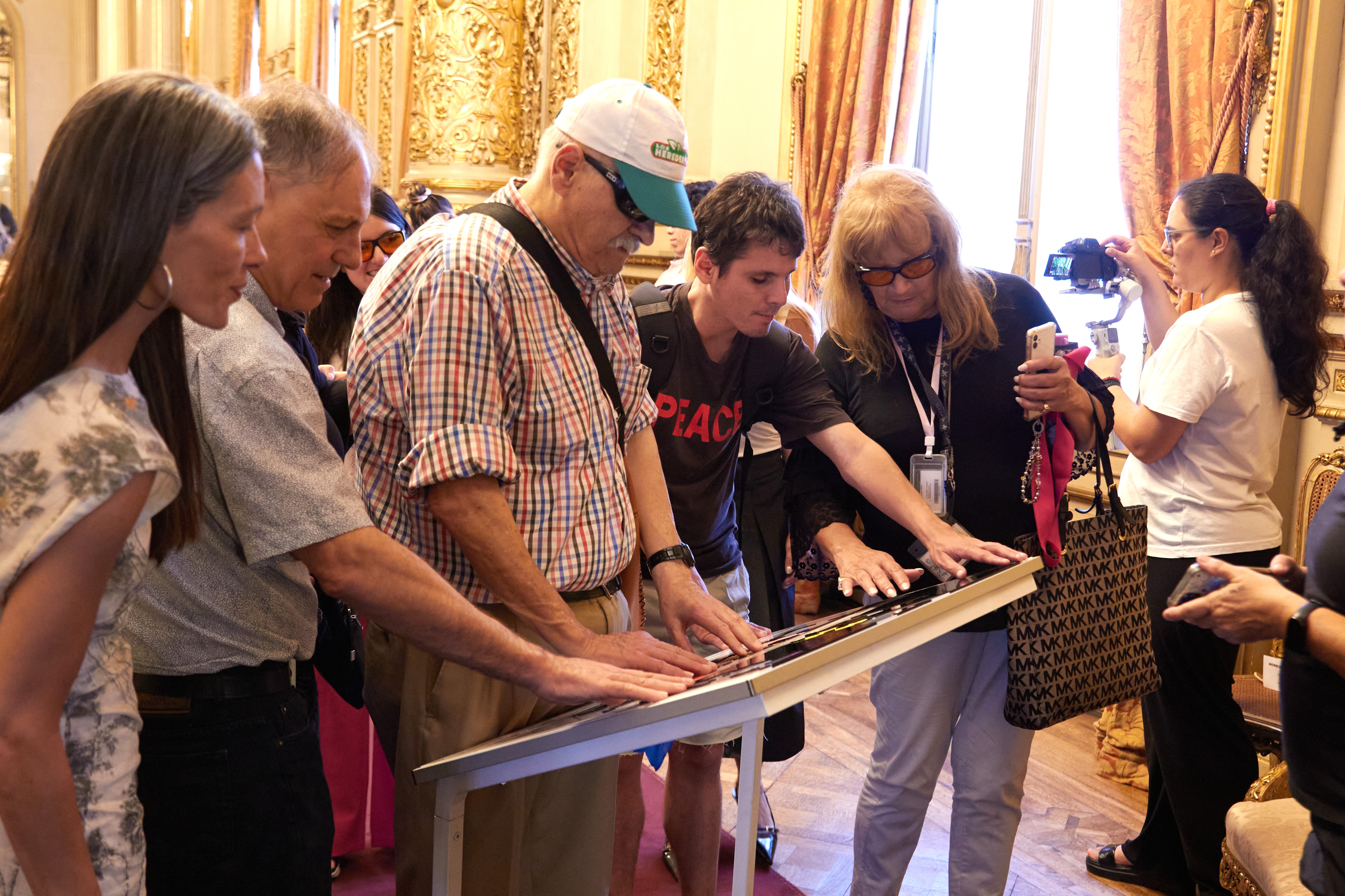 Un grupo de personas recorre con las manos un plano háptico instalado dentro del Teatro Colón durante una visita accesible.