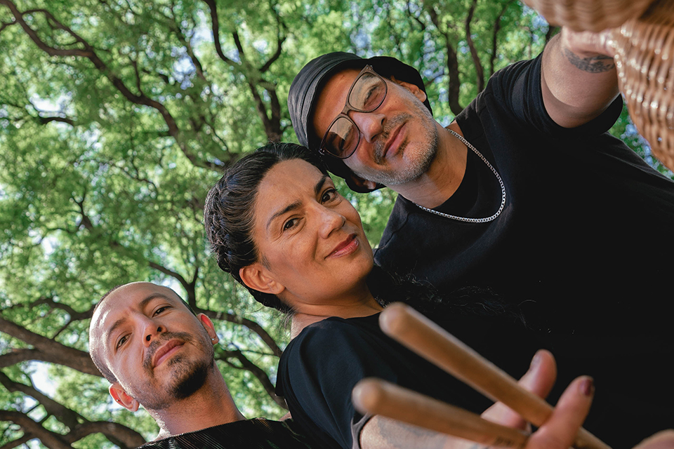 Los musicos Mariana Baraj, Leo Camargo y Marcelo Baraj posan con instrumentos sobre un fondo de arboleda verde