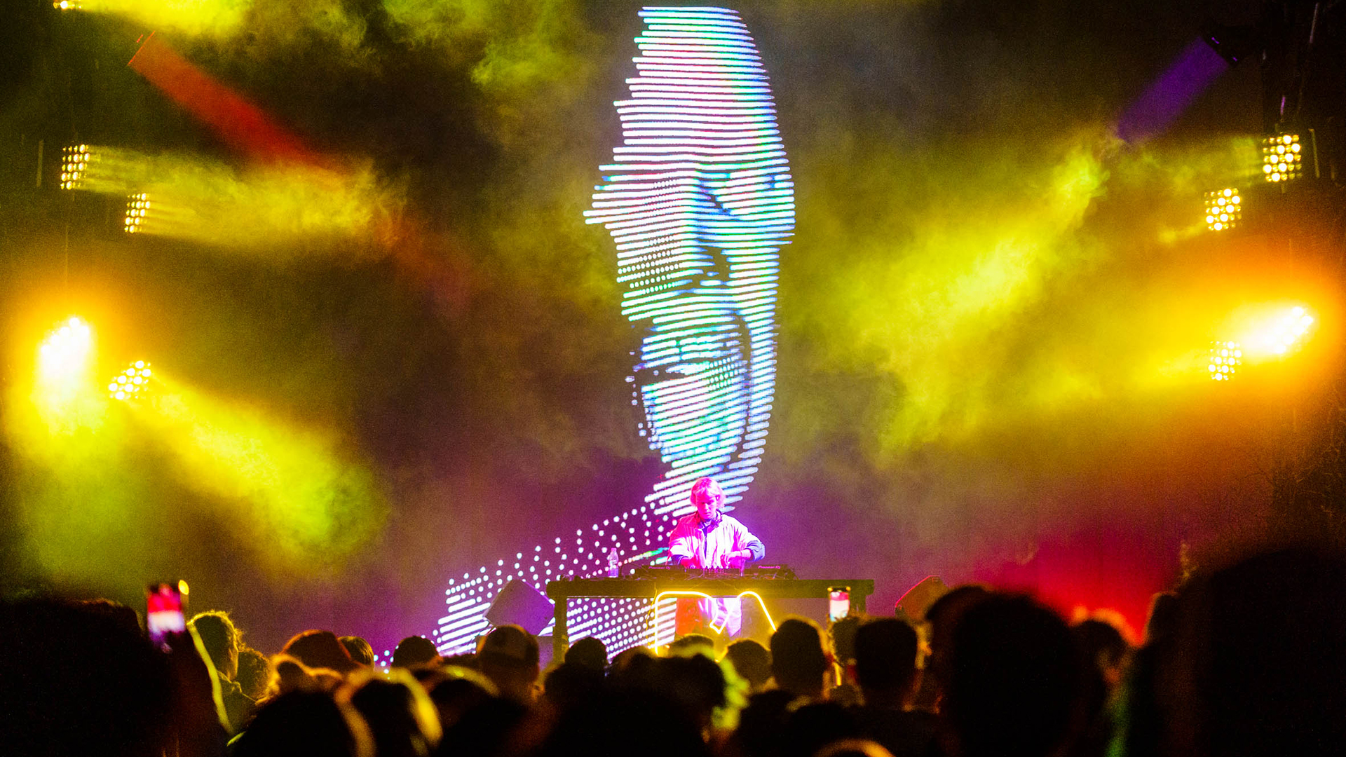 Dj tocando en escenario emergente con show de visuales y luces