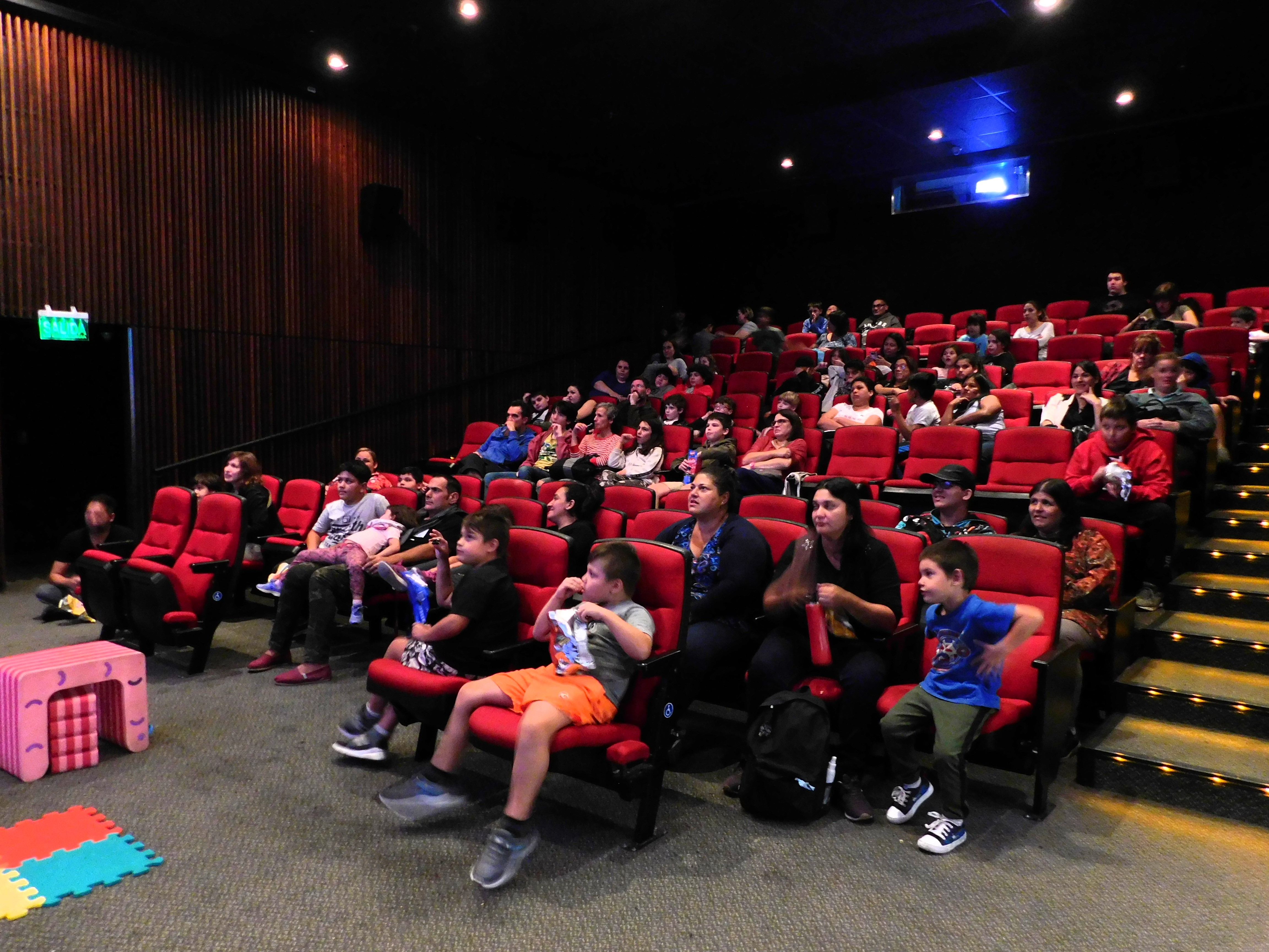Fotografia tomada dentro de la sala donde se observan a los espectadores sentados y rescotados en las sillas observando el espectaculo
