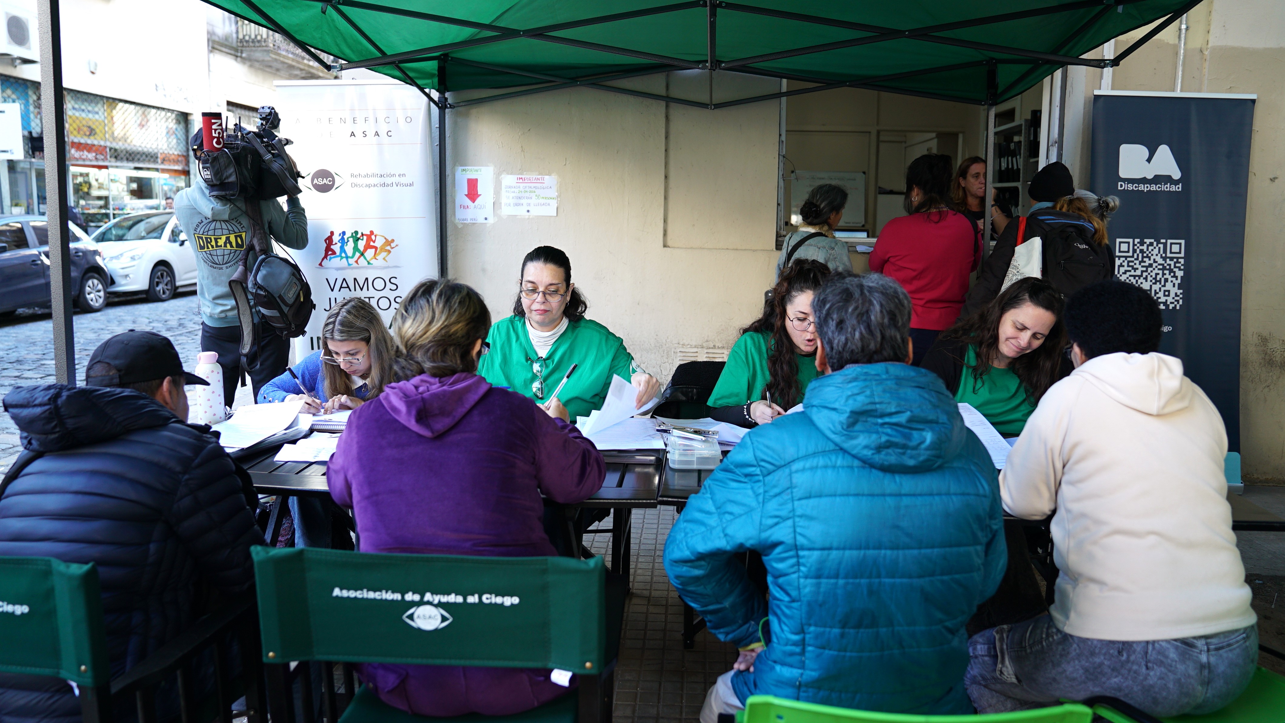 Jornada de atención oftalmológica con entrega de anteojos organizada por BA Discapacidad y ASAC, con personas realizando trámites y controles bajo una carpa en la vía pública.