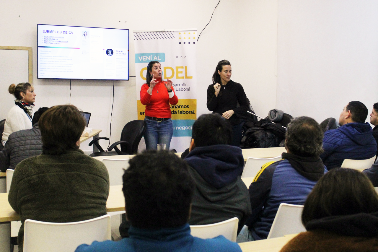 Taller de entrevistas simuladas para personas con discapacidad con apoyo de intérpretes de Lengua de Señas Argentina mientras se proyecta material sobre armado de CV y una oradora brinda explicaciones