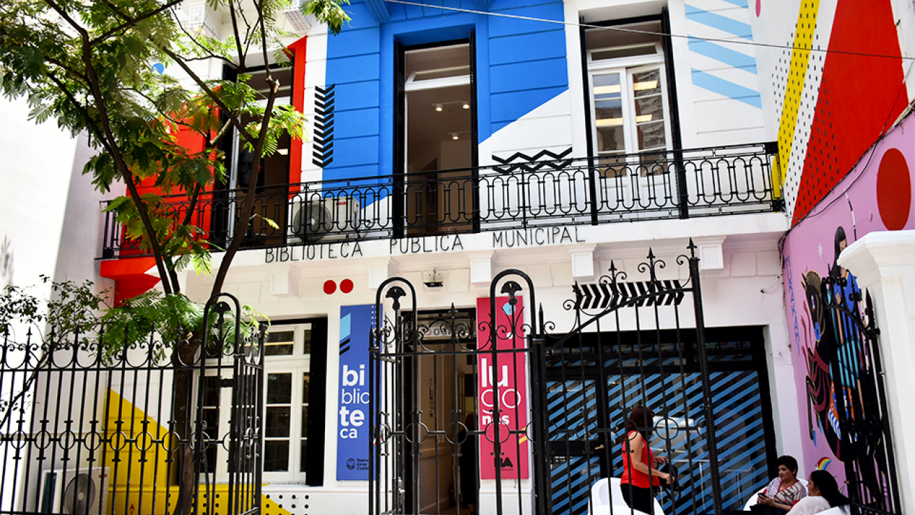 Frente de una casa de dos plantas, las paredes estan en color blanco con algunos adornos de varios colores 
