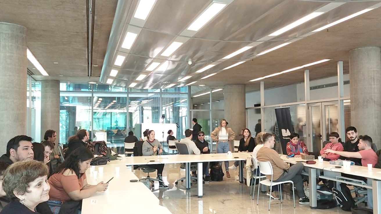 Grupo de participantes en la Jornada de Foto-Producto alrededor de mesas largas en una sala moderna de la sede del Gobierno de la Ciudad.