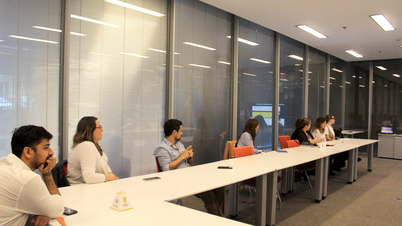 Varios participantes en una reunión, escuchando atentamente en una sala de trabajo bien iluminada