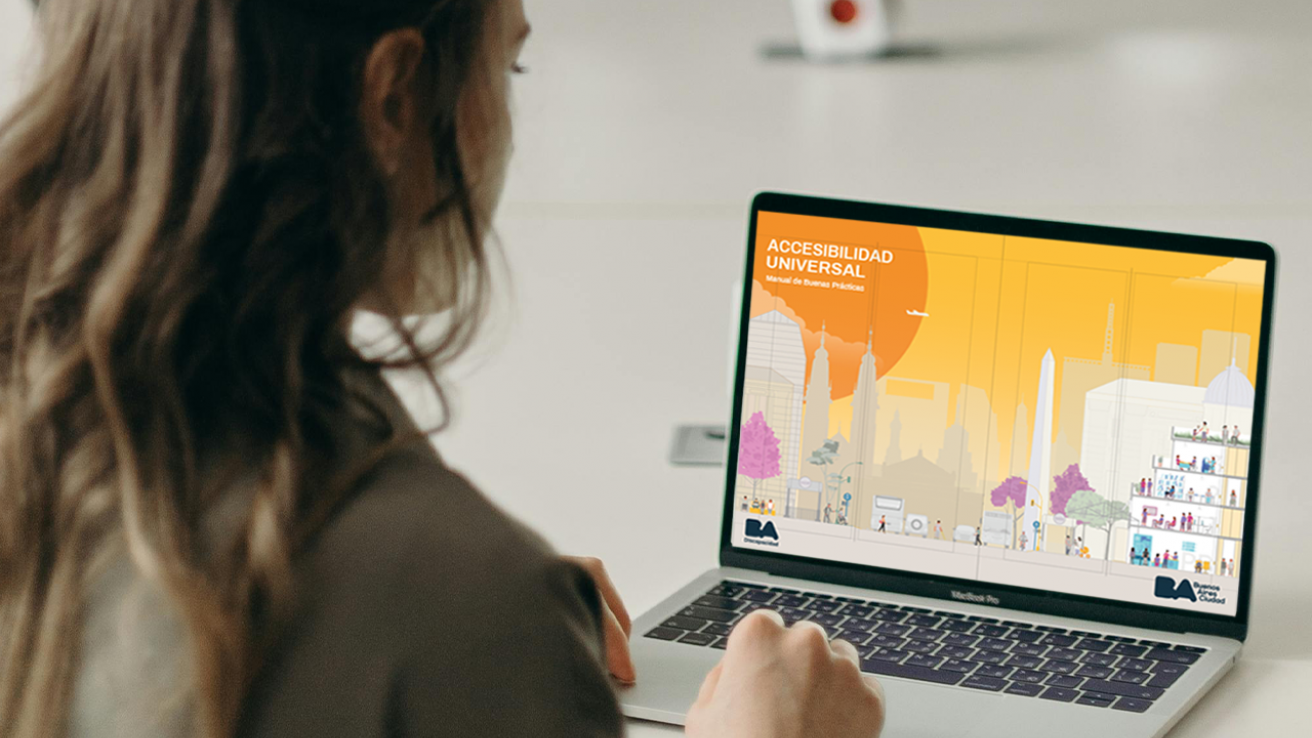 Persona frente a una computadora portátil observando la portada del “Manual de Buenas Prácticas en Accesibilidad Universal” del Gobierno de la Ciudad de Buenos Aires.