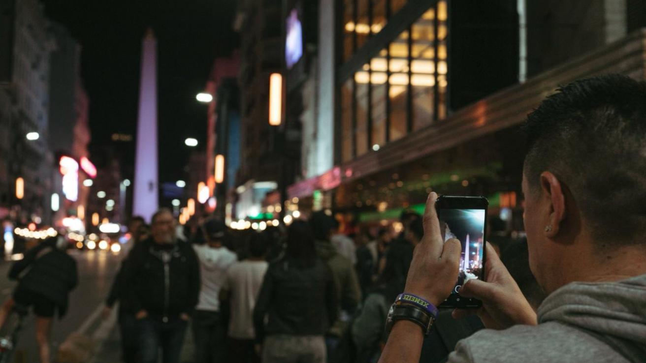 Persona sacandole foto al Obelisco. Calle Corrientes llena de gente de noche