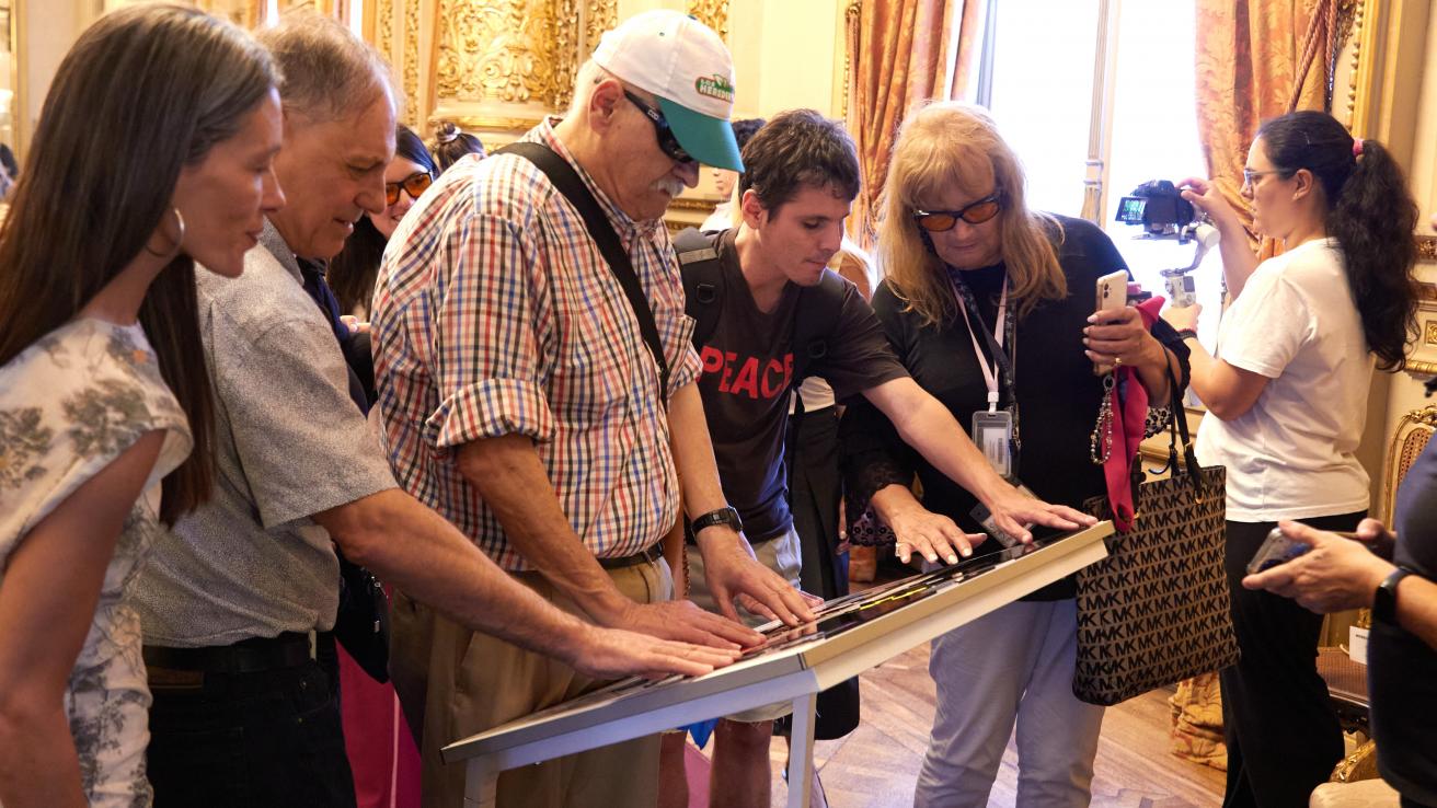 Un grupo de personas recorre con las manos un plano háptico instalado dentro del Teatro Colón durante una visita accesible.
