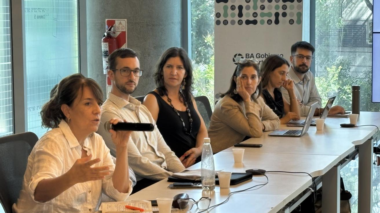 Mujer hablando con un micrófono sentada en una mesa con otras personas