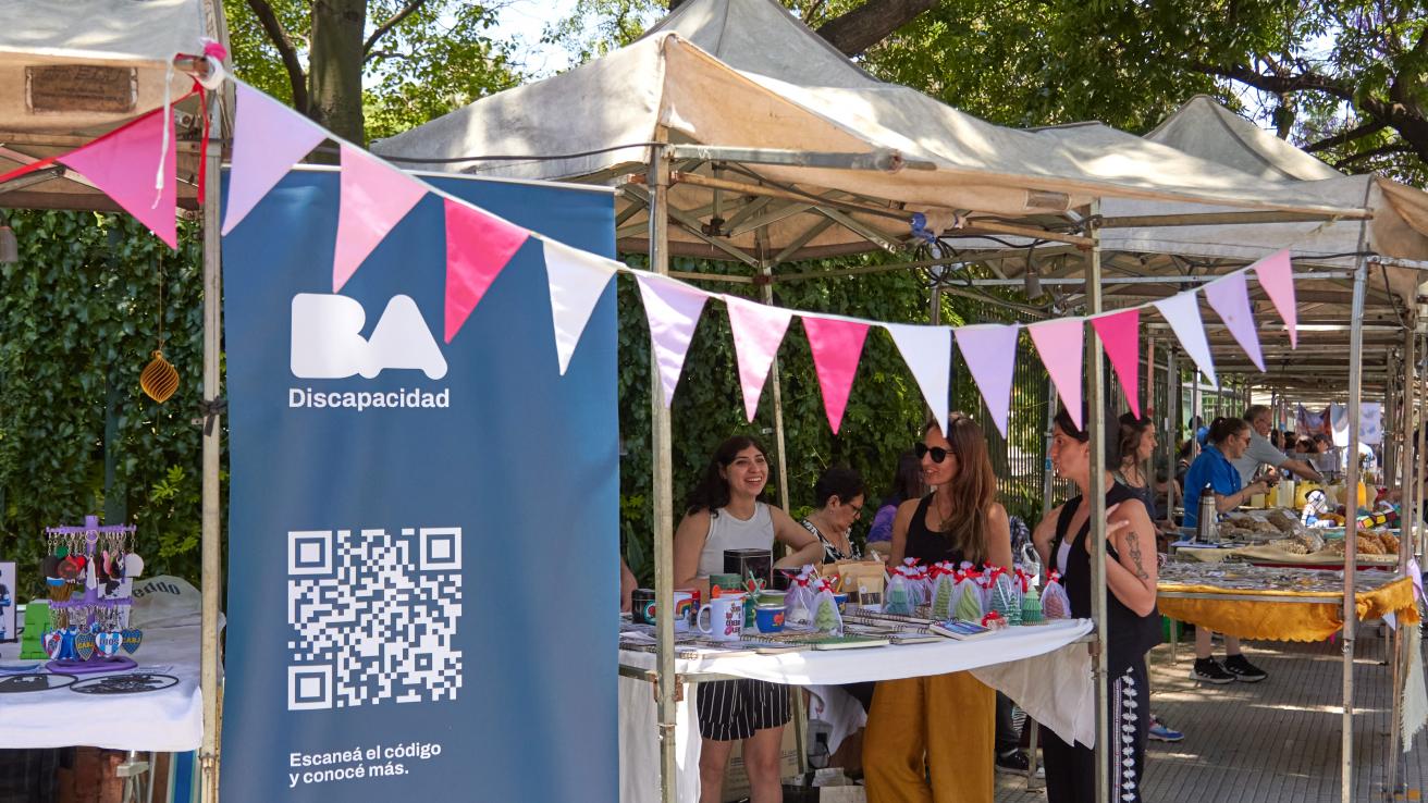 Puesto de emprendedores con discapacidad en una feria al aire libre, con productos artesanales exhibidos y un banner de BA Discapacidad.