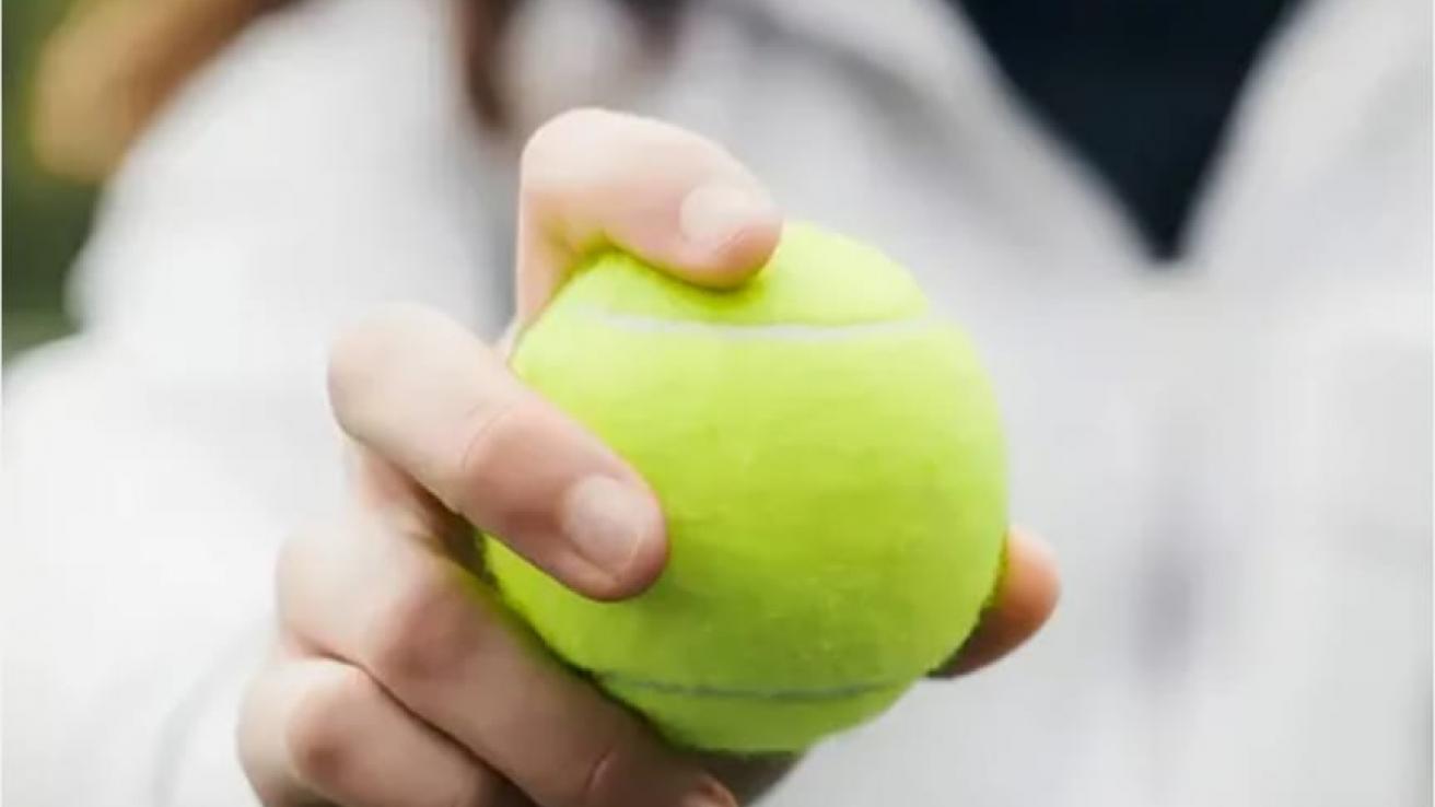 Una mano sostiene una pelota de tenis verde, símbolo de la campaña que promueve aulas más accesibles y amigables.