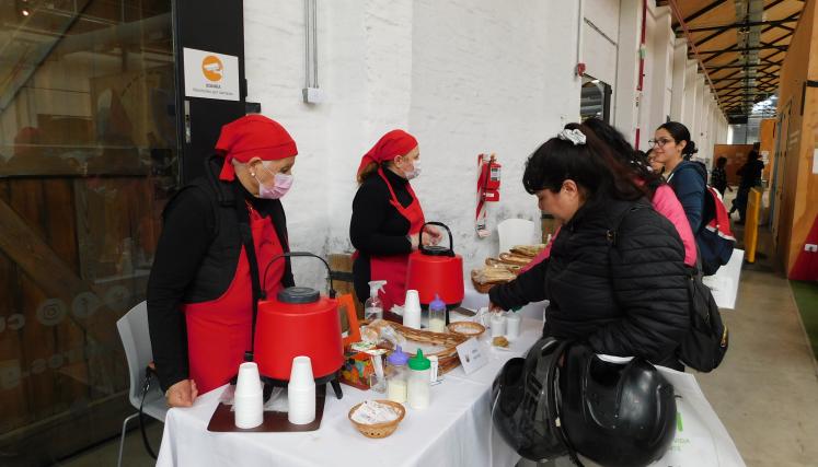 Fotografía donde aparece la mesa del catering, sus colaboradores y personas degustando. 
