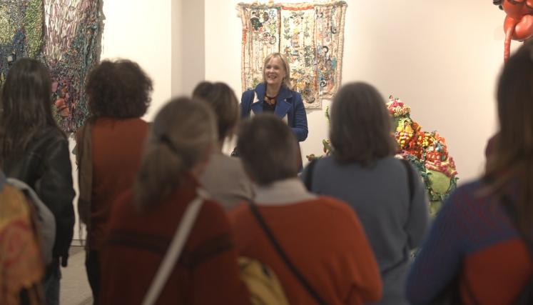 En la imagen se ve en el centro una artista sonriendo mientras habla a un grupo de personas que la escucha atentamente