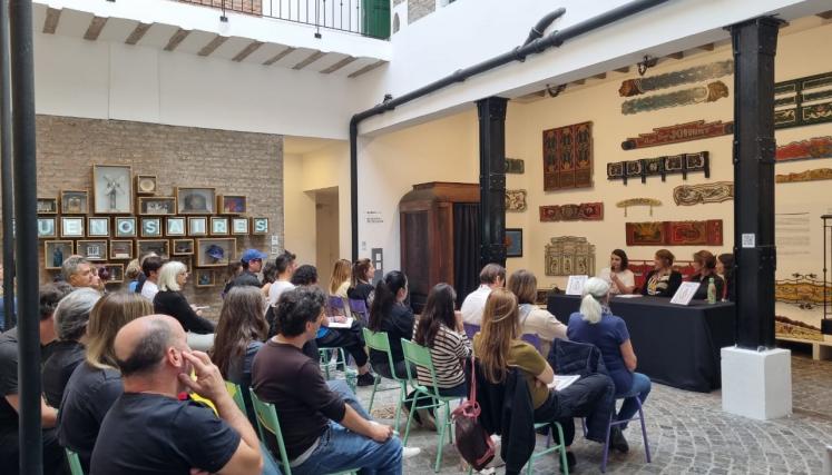 Fotografía del patio del museo durante la presentación del catálogo. Se observa una gran cantidad de personas sentadas, prestando atención a los anfitriones del evento, quienes presentan un catálogo de fileteado porteño.