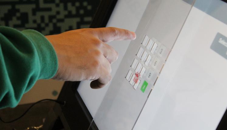 Persona utilizando la pantalla táctil de una máquina de votación con boleta única electrónica durante el proceso electoral.