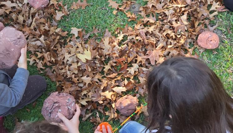 Ronda de niños y niñas que están sentados en un jardín alrededor de un círculo de hojas otoñales