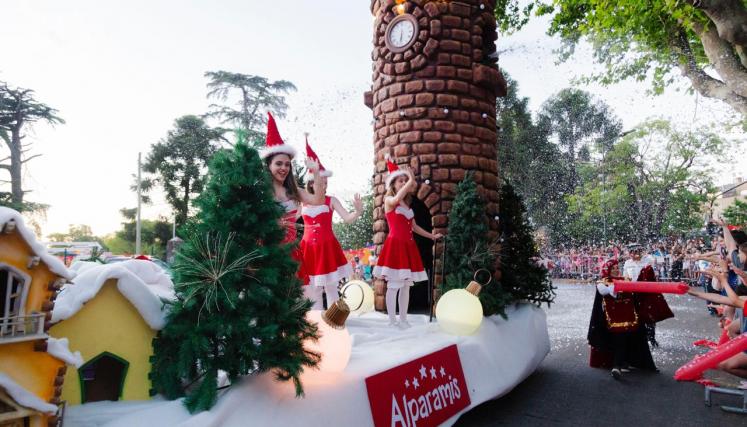 Desfile con arboles, casitas con nieve y mujeres vestidas de Papá Noel