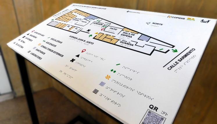 Plano táctil accesible con información en braille, íconos y señalización del edificio indicando sectores como guardia, sala de espera, escaleras y ascensor.