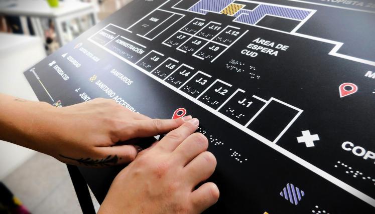 Persona explorando con las manos un plano háptico con información en braille para orientación dentro del edificio.