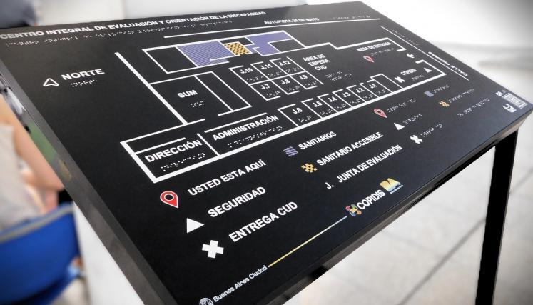 Plano háptico accesible instalado sobre atril, con señalización en braille y pictogramas para la orientación dentro del edificio.