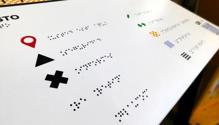 Plano táctil accesible con información en braille, íconos y señalización del edificio indicando sectores como guardia, sala de espera, escaleras y ascensor.